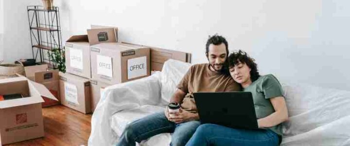 Umzugskosten clever steuern: Mit Strategie entspannt ins neue Zuhause A couple sits together on a couch, using a laptop amidst moving boxes, enjoying relaxed time indoors., tags: umzugskosten clever steuern: - pexel