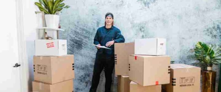 Strategische Umzugsplanung: Umzugskosten effektiv managen Smiling mover in coveralls standing with parcels, clipboard in hand, indoors., tags: umzugskosten - pexel